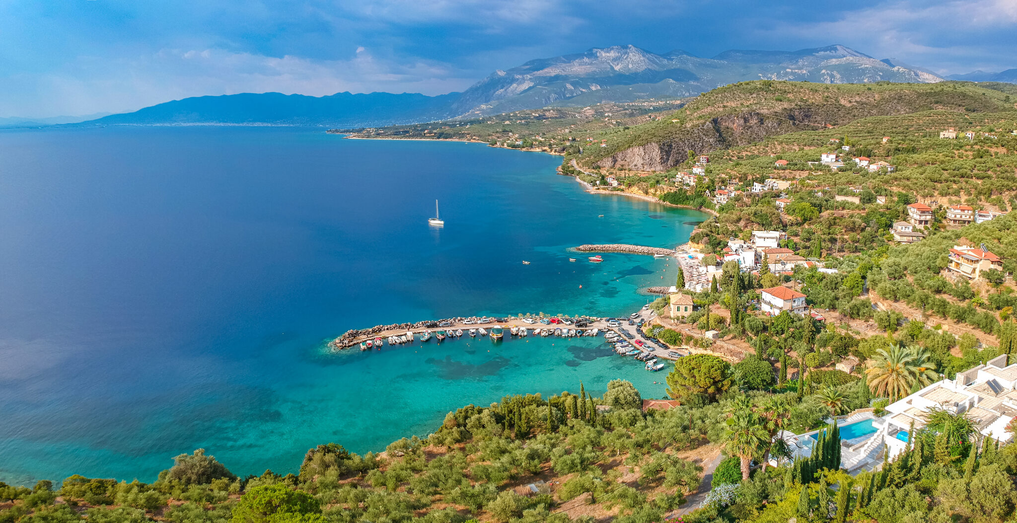 Charming Greek harbor village with traditional red-roofed buildings and yachts in turquoise waters