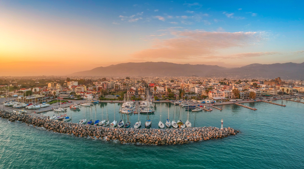 Aerial view of Kalamata marina at sunset with sailboats moored along the breakwater and the city in the background